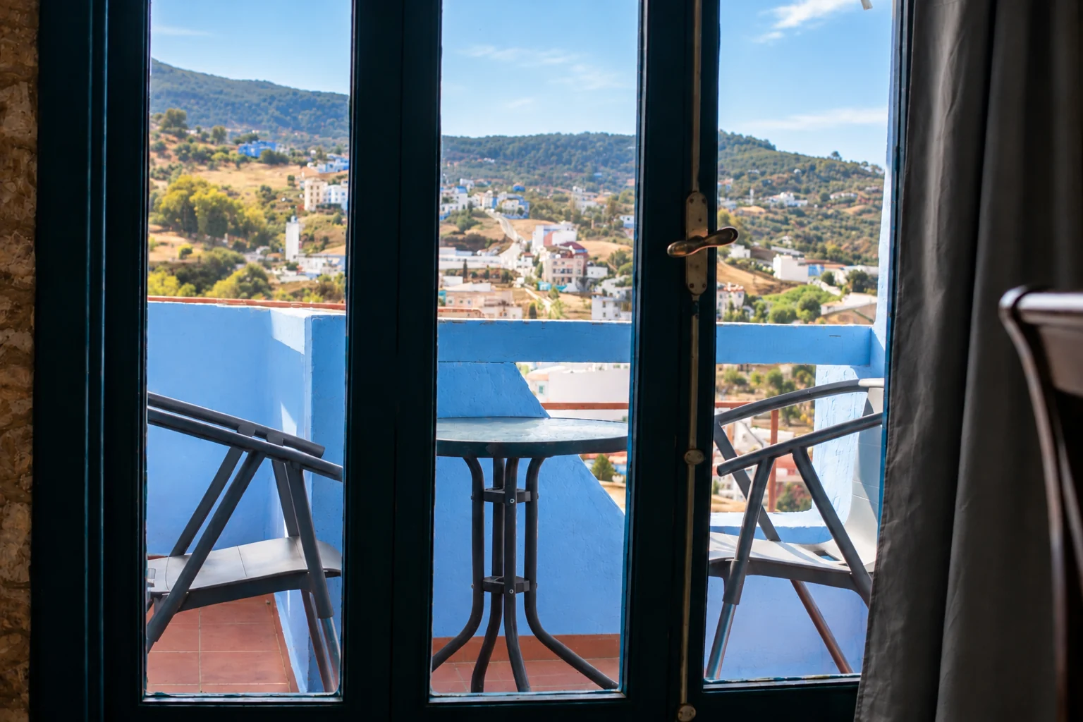 Terraza azul con mesa y sillas, vista a través de puertas de cristal.
